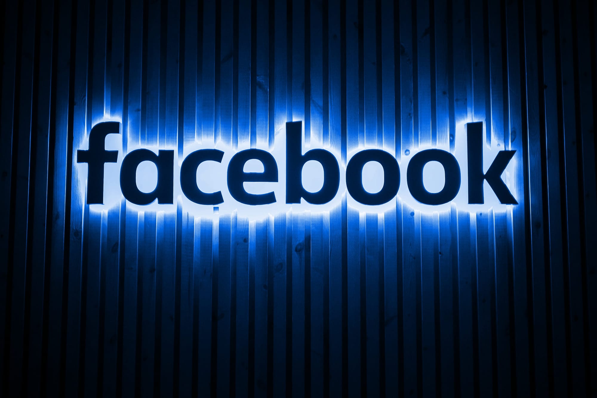 The Facebook logo, backlit in blue on a textured wall