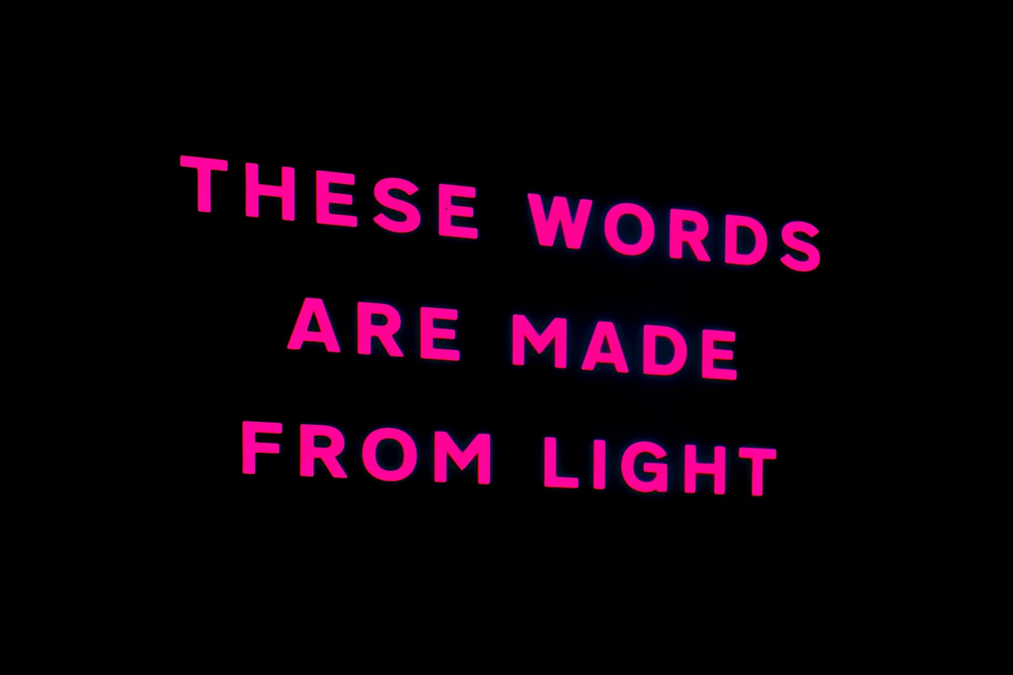 THESE WORDS ARE MADE FROM LIGHT projected onto a black wall