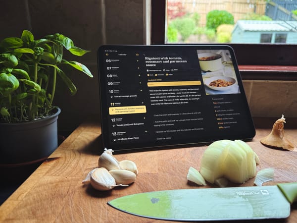 iPad with Mela app showing recipe and calendar next to garlic, onion, knife, and basil plant