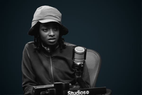 Black and white photo of Little Simz in a bucket hat at a podcast mic in studio.